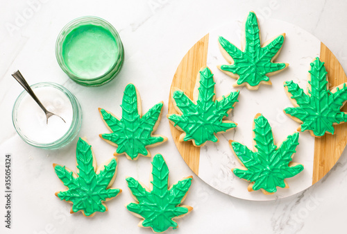 Cannabis cookies overhead on white marble. THC or CBD baking weed cookies flat lay. Cannabis edibles for medical or recreational consumption. Made with cannabis infused oil and royal icing.
