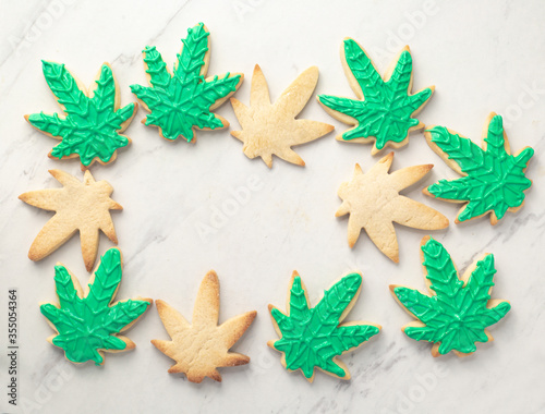 Fototapeta Naklejka Na Ścianę i Meble -  Cannabis cookies overhead on white marble. THC or CBD baking weed cookies flat lay. Cannabis edibles for medical or recreational consumption. Made with cannabis infused oil and royal icing.