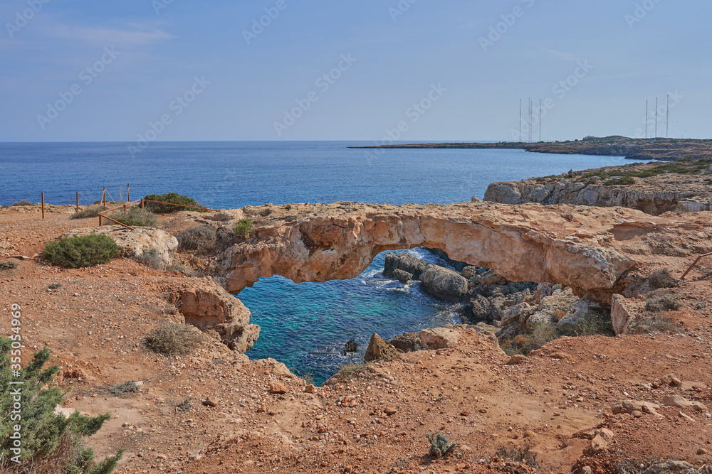 view of the natural stone Love Bridge in Cyprus, red yellow sandstone with a view of the turquoise blue water and the horizon with blue sky on a sunny day,  ayia napa