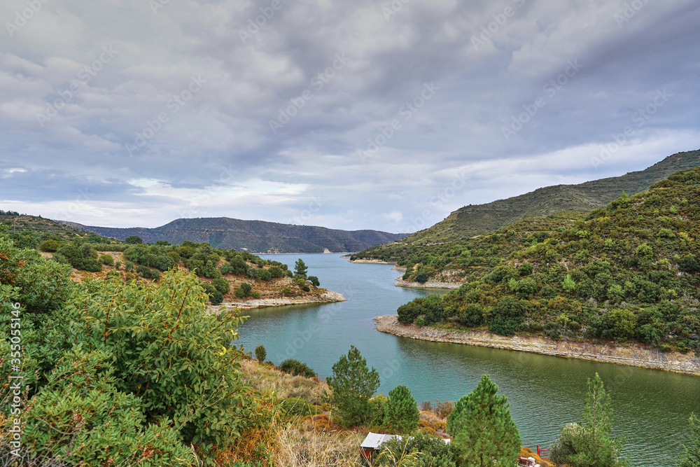 View of a beautiful deserted lake or river in the mountains on the island of Cyprus. blue water, green plants and trees and a slightly cloudy sky