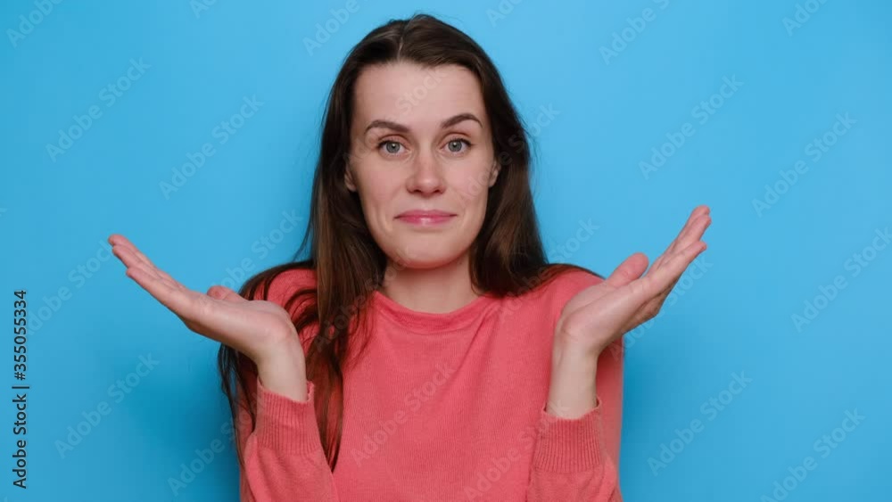Confused young woman imagining alternatives spreads palms, feels hesitant and doubtful, has no clue, wears red sweater, looks with questioned expression, isolated over blue studio background Confused young woman imagining alternatives spreads palms, feels hesitant and doubtful, has no clue, wears red sweater, looks with questioned expression, isolated over blue studio background
