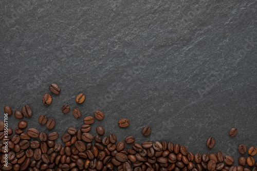 Top view above of coffee beans brown roasted on dark stone table background. The raw material of breakfast menu for is drink has pleasant aroma and freshness from caffeine. Flat lay with copy space.