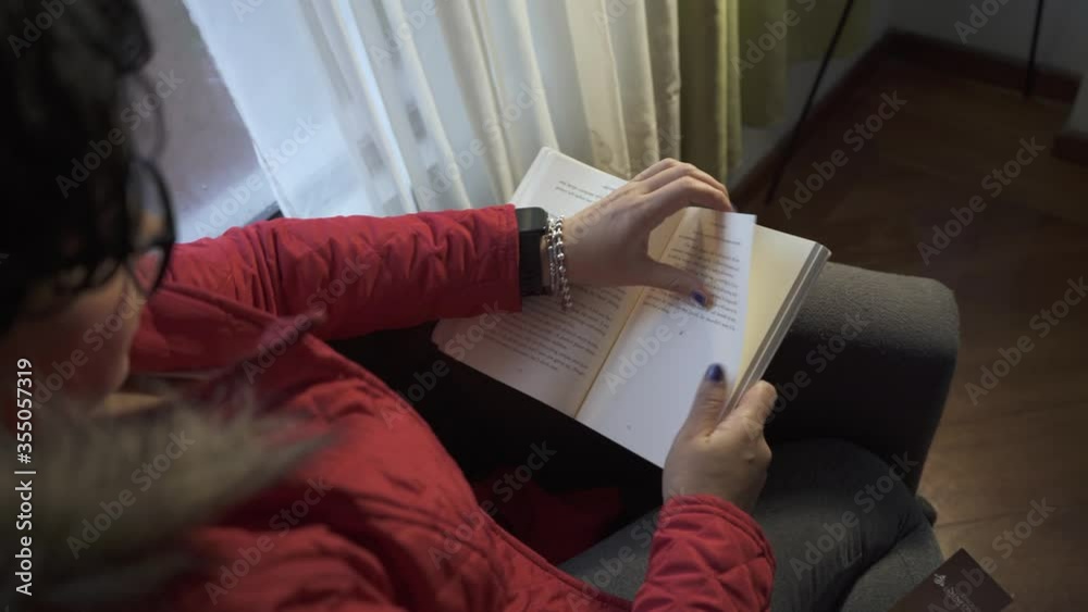 Mujer leyendo un libro, da vuelta a la página y termina un capítulo. Deja de leer y mira  a través de la ventana, al final empieza a reflexionar.