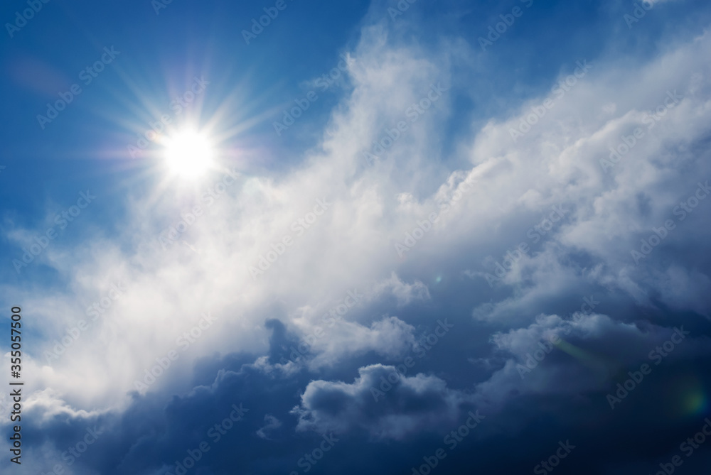 Fototapeta premium bright natural sun behind dramatic dark clouds in blue sky