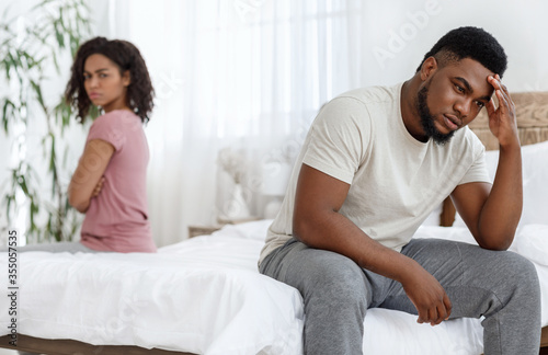 Young black couple having relationships crisis, sitting separated on bed