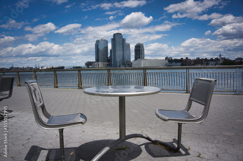 Chairs and table on a promenade along East River in Manhattan with a view of Brooklyn