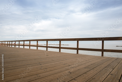 a wooden fence at a boardwalk at the seaside with the sea visible in the background © SockaGPhoto
