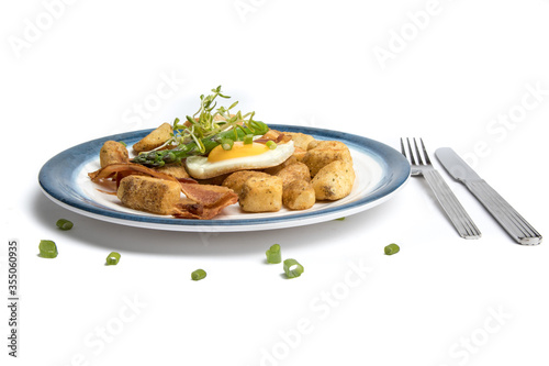 a fried egg sunny side up on a blue plate with potatoes bacon asparagus and bread isolated on white