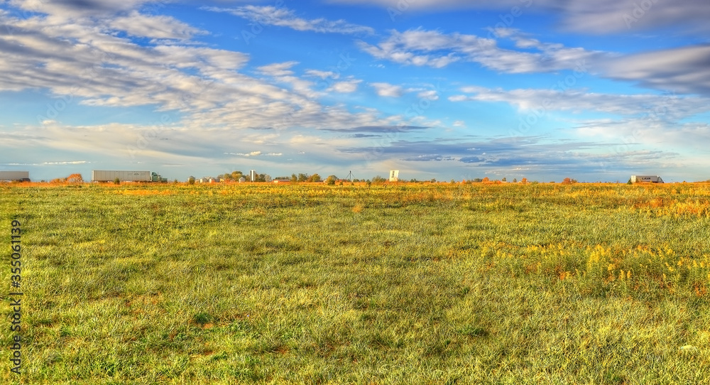 Obraz premium semi trucks moving across the prairie state with golden hued green fields beneath a blue and white cloudy sky, Highway 55, Litchfield Illinois 