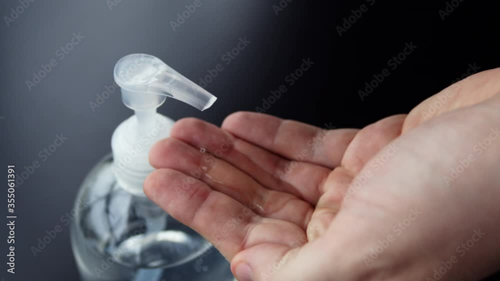 Cleaning hands with hand sanitizer sanitiser gel used for hygiene and keeping hands clean to prevent virus spread. Man washing hands using alcohol based fluid. Top close up view on black background.