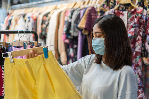 woman choosing clothes at shopping mall and her wearing medical mask for prevention from coronavirus (Covid-19) pandemic. new normal concepts