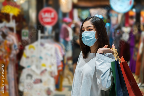 woman holding shopping bag and looking to clothes at mall and her wearing medical mask for prevention from coronavirus (Covid-19) pandemic. new normal concepts © geargodz