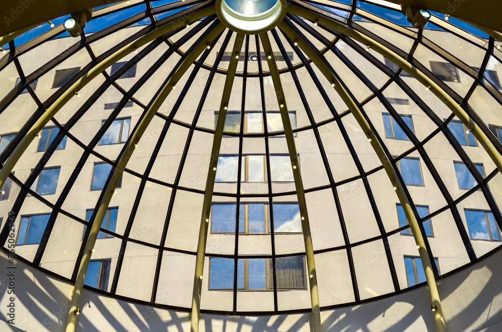 View through the glass dome roof of modern corporate building with windows and sky reflections.