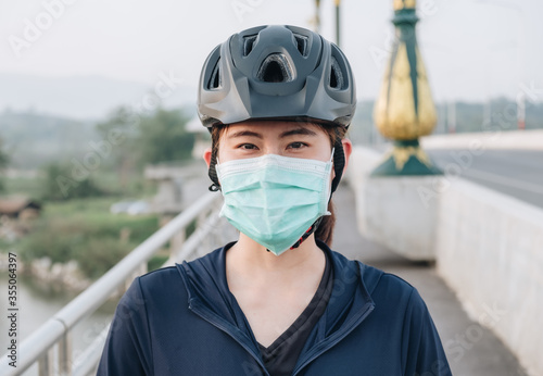 Portrait of young woman wearing a mask while riding a bicycle outdoor for protect and prevent the spread of virus. Conceptual of new normal lifestyle, everybody should wearing a mask when go outdoor. © boyloso