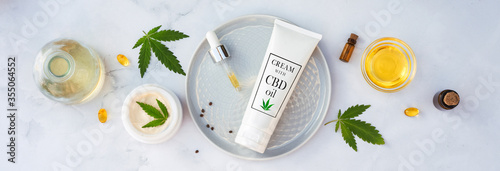 Tuba and jar of cream CBD oil, THC tincture and hemp leaves on marble background. Flat lay, minimalism. Cosmetics CBD oil. Cream with hemp oil and marijuana leaves photo