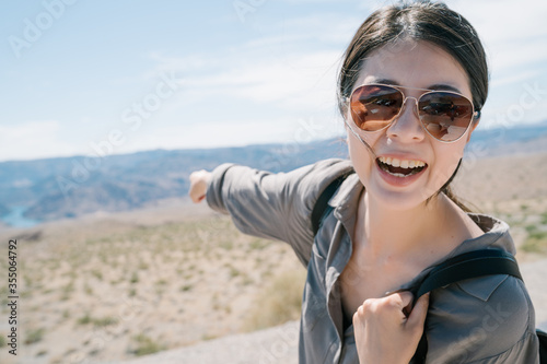 excited vlogger traveling to arid region pointing and introducing distinctive landscape to fans. japanese woman tourist face to camera thrilled to see wild nature in desert area from top.....