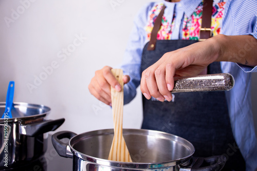 An unrecognizable woman cooking and adding ingredients to a meal