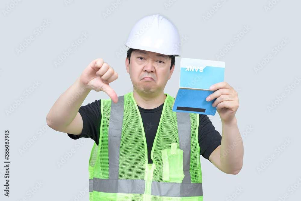 A middle-aged Asian engineer holding a bank passbook in his hand on a gray background. A middle-aged Asian engineer holding a bank passbook in his hand on a gray background.