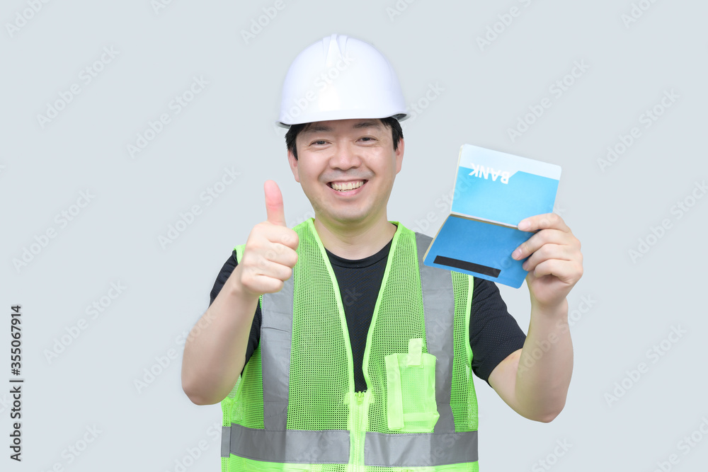 A middle-aged Asian engineer holding a bank passbook in his hand on a gray background. A middle-aged Asian engineer holding a bank passbook in his hand on a gray background.