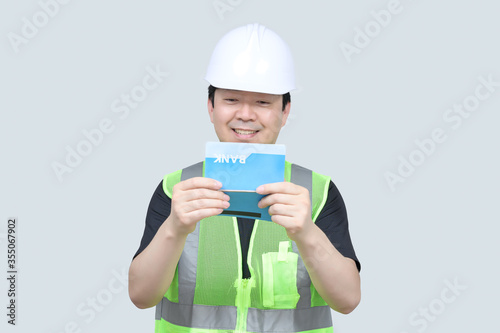A middle-aged Asian engineer holding a bank passbook in his hand on a gray background.