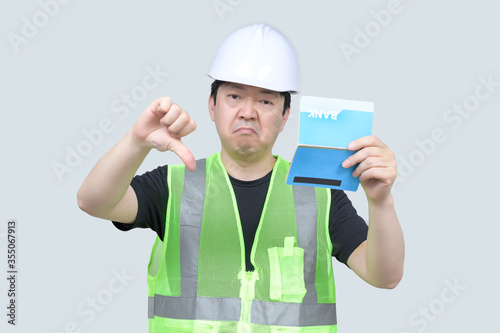 A middle-aged Asian engineer holding a bank passbook in his hand on a gray background.