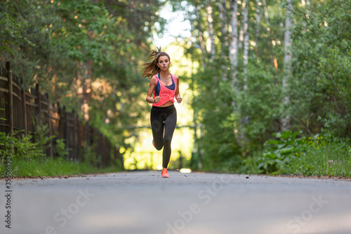 Sportswoman runs along the road in the forest.