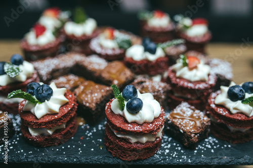 Chocolate biscuit cakes with whipped cream blueberry - strawberry and mint leaf topping served on black slate