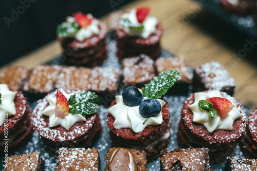 Chocolate biscuit cakes with whipped cream blueberry - strawberry and mint leaf topping served on black slate