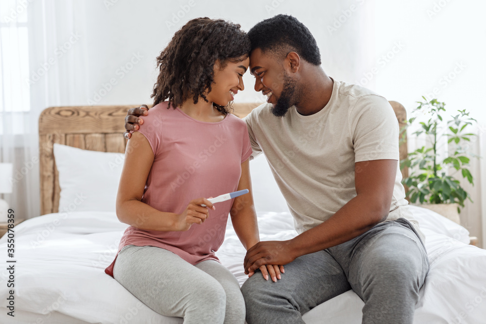 Happy black couple holding positive pregnancy test on bed Happy black couple holding positive pregnancy test on bed