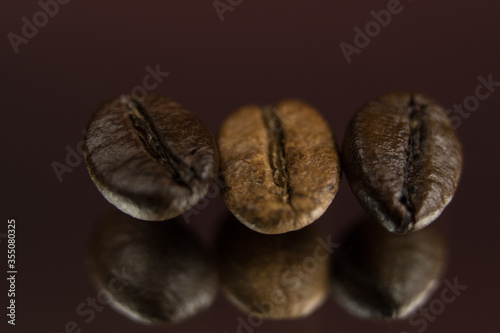 Three roasted coffee beans in a row, horizontal. Extreme close up, macro photography, selective focus. Background deep red, foreground textured black with light effects. Space for copy or text. © stockyes