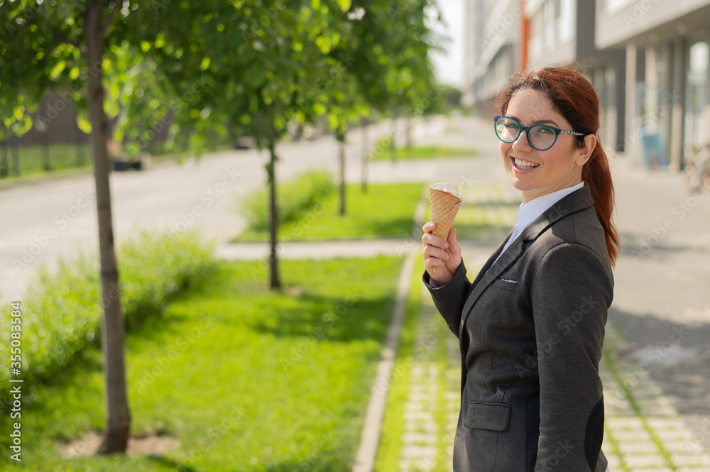 Business woman walks outdoors and enjoys vanilla ice-cream. Happy girl in a suit eats an ice cream cone on a hot sunny summer day. Lunch break of an office employee. Business woman walks outdoors and enjoys vanilla ice-cream. Happy girl in a suit eats an ice cream cone on a hot sunny summer day. Lunch break of an office employee.