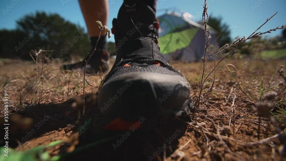 Man stepping on tent stake close up at campsite to pitch his tent and secure it into the ground