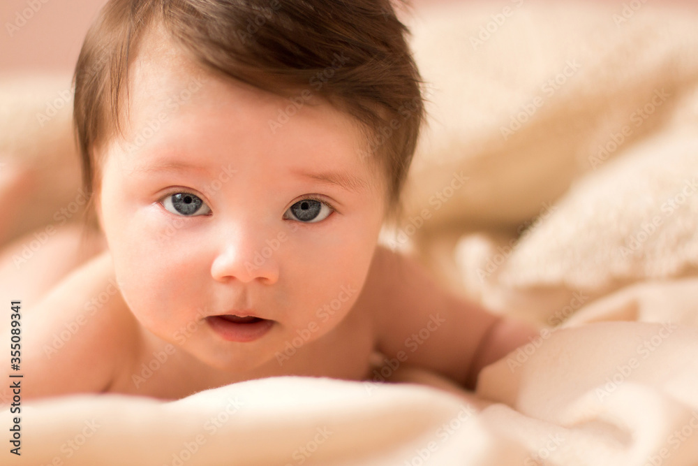 Portrait of adorable smiling newborn baby with thick brown hair . Nude newborn child relaxing in bed. Portrait of adorable smiling newborn baby with thick brown hair . Nude newborn child relaxing in bed.