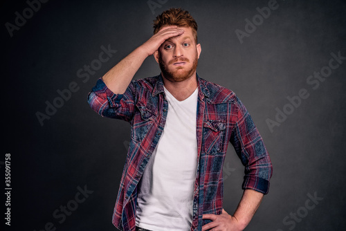 Phew, almost caught. Portrait of cute tired guy with red hair feelling relieved, whiping sweat out of forehead, gazing aside with exhausted expression, overcoming all troubles and breathing out photo