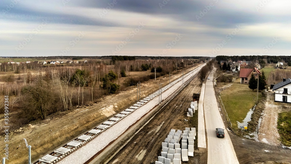 Fototapeta premium Zabiezki, Poland, 2020. Aerial view on railway line construction site in small village near Otwock and Warsaw. Railway components ready to deploy. Train tracks underlay and concrete ties.