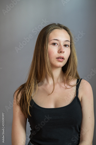 Portrait of a charming young woman wearing a camisole posing looking at the camera on grey background