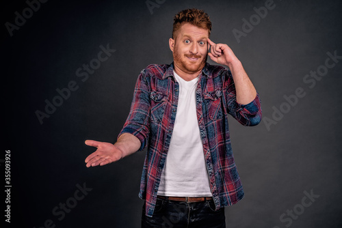 Man mocking friend who made stupid mistake. Portrait of confused and displeased handsome redhead caucasian guy rolling index finger on temple and pointing with palm at camera, acting crazy or dumb