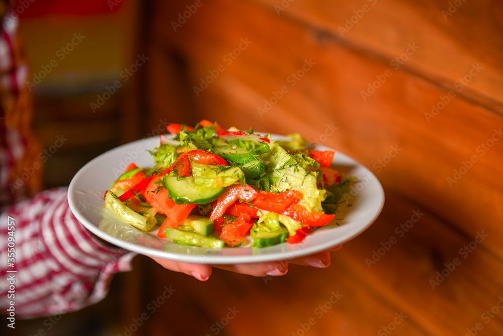 Waiter serving vegetable salad with juicy tomatoes, lettuce, radish, cucumber. Restaurant service.
