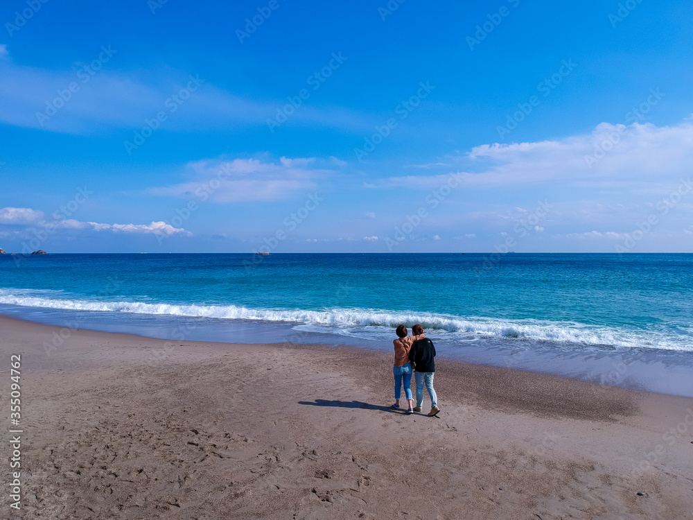 ドローンで空撮した冬の海の砂浜で散歩しているカップル
