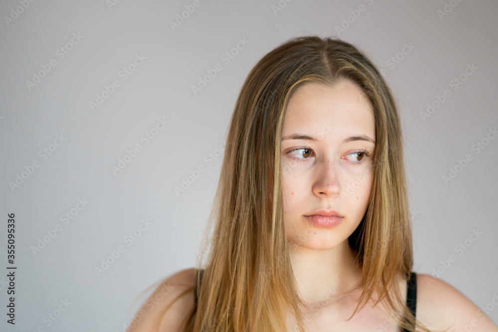 Close up portrait of a beautiful and pensive young woman with a sulky face on a grey background Close up portrait of a beautiful and pensive young woman with a sulky face on a grey background
