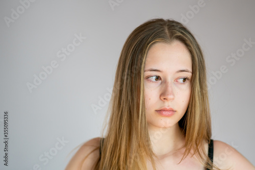 Close up portrait of a beautiful and pensive young woman with a sulky face on a grey background