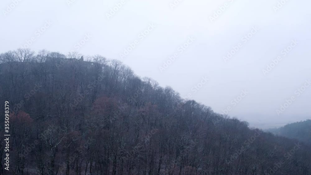 Aerial panning shot of structure on hill amidst bare trees against sky, drone flying over forest during winter - Thuringia, Germany Aerial panning shot of structure on hill amidst bare trees against sky, drone flying over forest during winter - Thuringia, Germany
