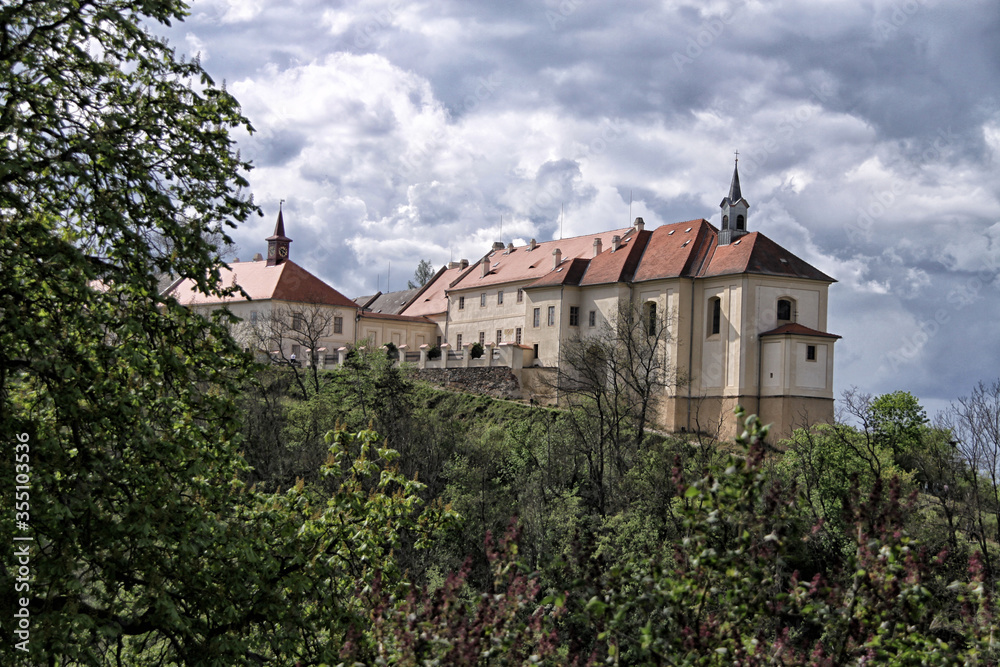 Nizbor castle over green trees in day with heavy clouds