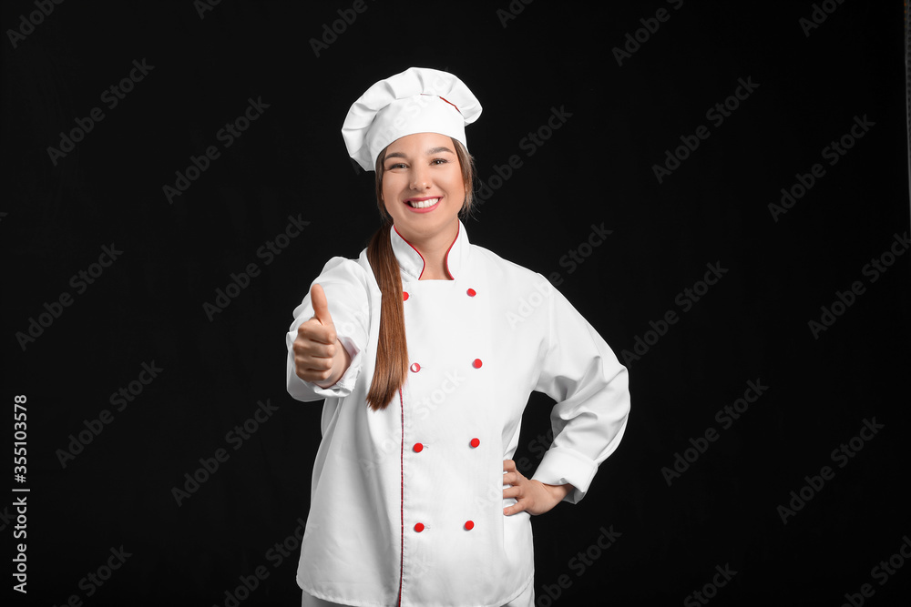 Young female chef showing thumb-up on dark background Young female chef showing thumb-up on dark background