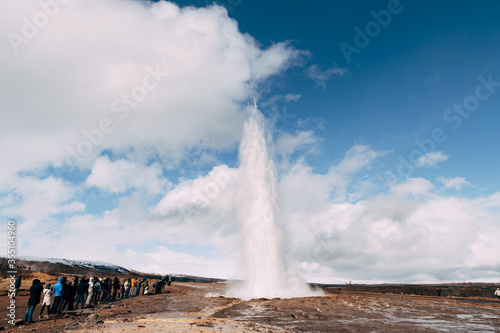 Geyser Valley in the southwest of Iceland. The famous tourist attraction Geysir. Geothermal zone Haukadalur. Tourists look at the eruption of Strokkur geyser on the slopes of Laugarfjall hill.