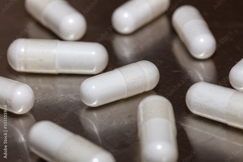 White pills scattered on scratched metal surface. Majority of the pills and much of the surface are in soft focus. Angled / close-up shot. Healthcare / hospital concept. White pills scattered on scratched metal surface. Majority of the pills and much of the surface are in soft focus. Angled / close-up shot. Healthcare / hospital concept.