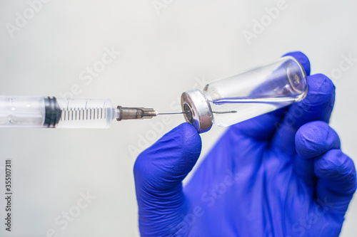 a hand in a blue medical surgical glove picks up a vaccine from an ampoule with the syringe