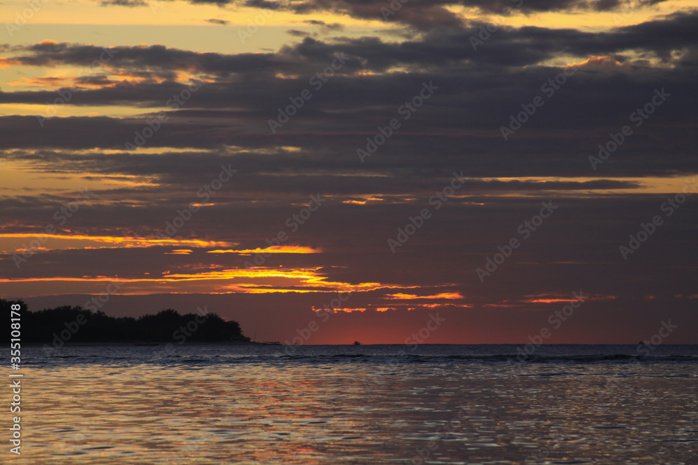 Sun behind clouds with exotic island silhouette