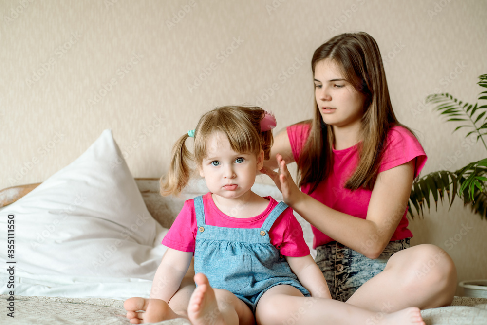 Children play on the bed in a bright bedroom. teen girl combing baby hair. funny girls. sisterly love. vacation home. Children play on the bed in a bright bedroom. teen girl combing baby hair. funny girls. sisterly love. vacation home.