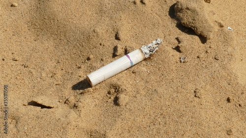 a half-smoked cigarette smoulders in the sand